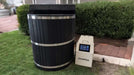 A black barrel-style Sawmill Structures Chiller Plunge with a ChillFlex cooling unit sits neatly on a green lawn near a home