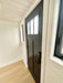 A black modern front door with vertical panels and glass panes stands inside Sawmill Structures Wanderlove Tiny Home