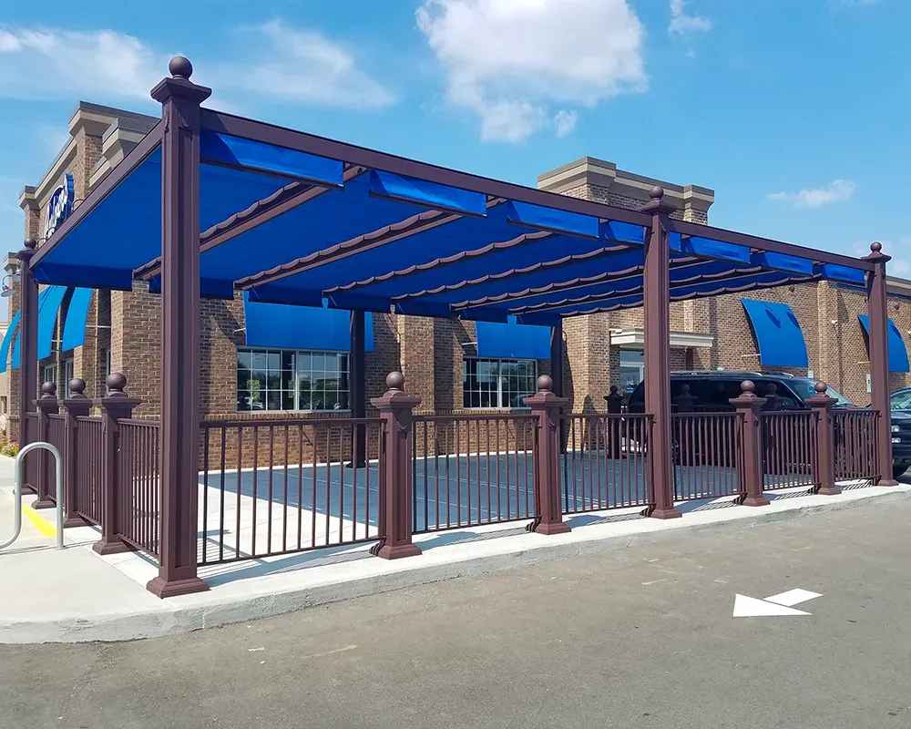 A blue-canopied outdoor seating area in front of a brick building, protected by a Structureworks Windsor Aluminum Patio Cover with matching awnings