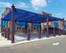 A blue-canopied outdoor seating area in front of a brick building, protected by a Structureworks Windsor Aluminum Patio Cover with matching awnings