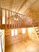 A bright, empty interior with tall walls, a wood ladder, and a railed loft showcases the spacious design of the Sawmill Structures The Jumbo Grand Loft 130 SD Garden Room