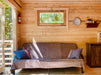 A brown-covered futon with blue and purple pillows sits under a small window inside the Sawmill Structures Edwin Lake House 70MM Garden Room