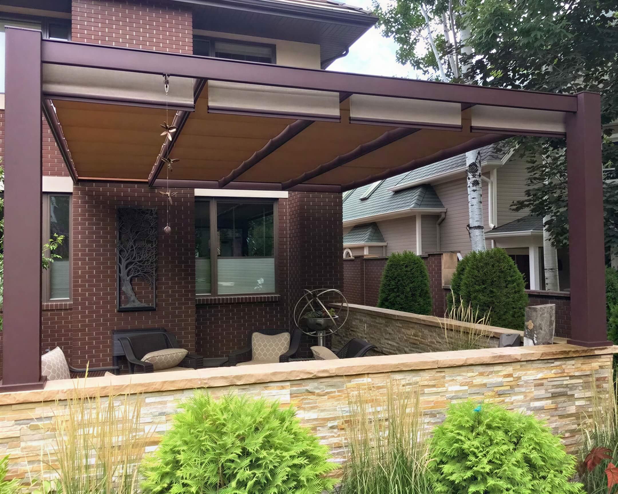 A brown Structureworks Outlook Aluminum Patio Cover & Pergola covers a cozy sitting area in a private courtyard surrounded by stone and brick walls