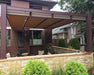 A brown Structureworks Outlook Aluminum Patio Cover & Pergola covers a cozy sitting area in a private courtyard surrounded by stone and brick walls