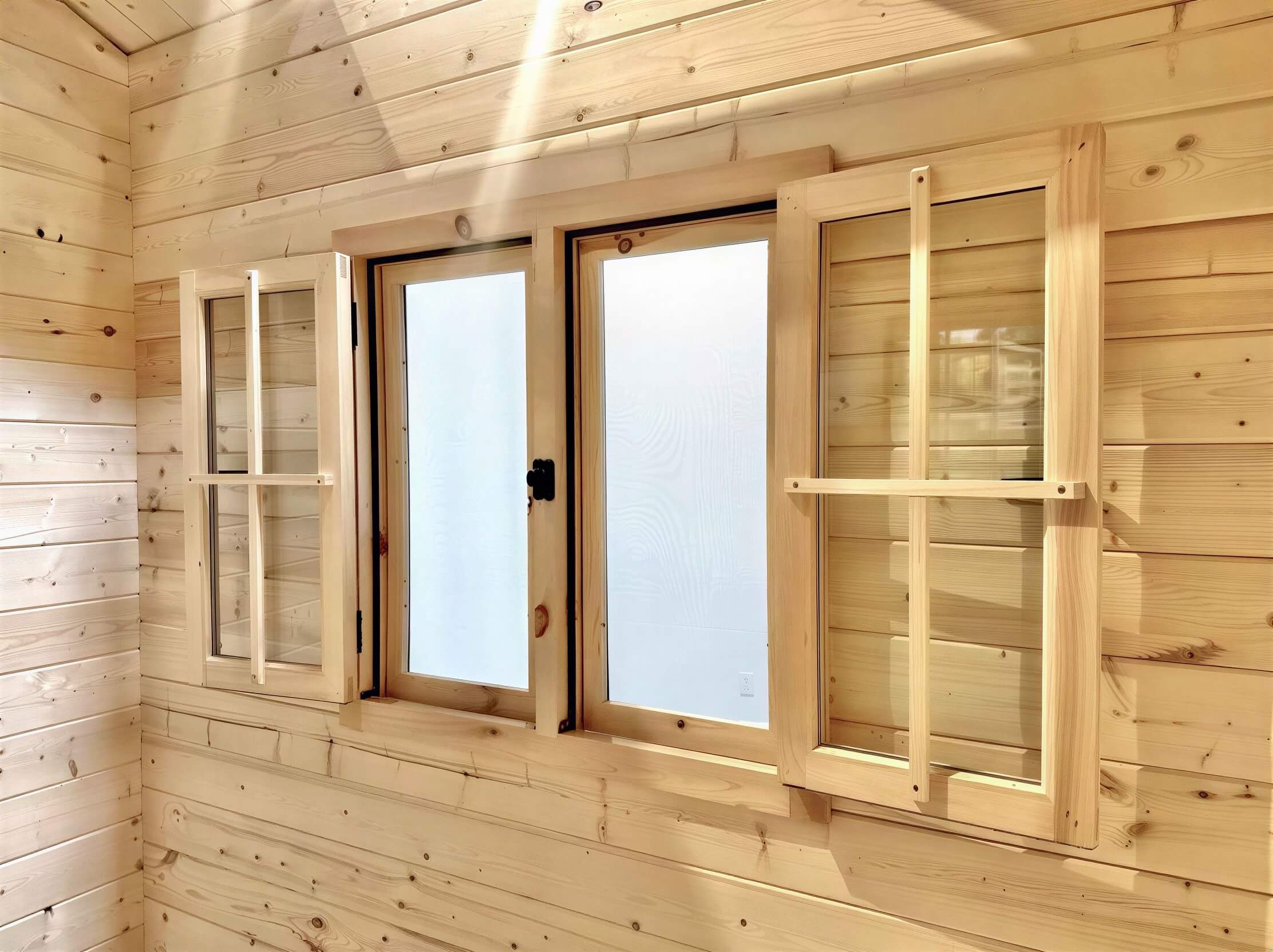 A close-up view of wooden-framed double windows with frosted glass and internal shutters inside the Sawmill Structures Harvest Grand Bungalow 107 Garden Room