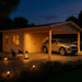 A cozy evening view of the GardenHouse24 USA Double Carport Erki 44 Garden Room with soft outdoor lighting and a car parked under the wooden shelter