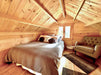 A cozy loft bedroom with a sloped wooden ceiling, soft lighting, and a green armchair is part of the Sawmill Structures The Jumbo Grand Loft 130 SD Garden Room