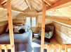 A cozy loft bedroom with sloped wooden ceilings, a full-size bed, accent pillows, and a green armchair is tucked inside the Sawmill Structures The Jumbo Grand Loft 130 SD Garden Room
