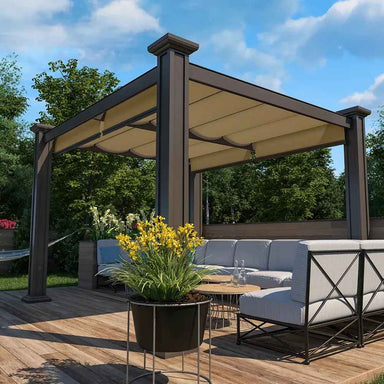 A cozy outdoor lounge with cushioned seating sits beneath a dark-framed, cream-canopied Structureworks Craftsman Aluminum Patio Cover & Pergola in a lush garden