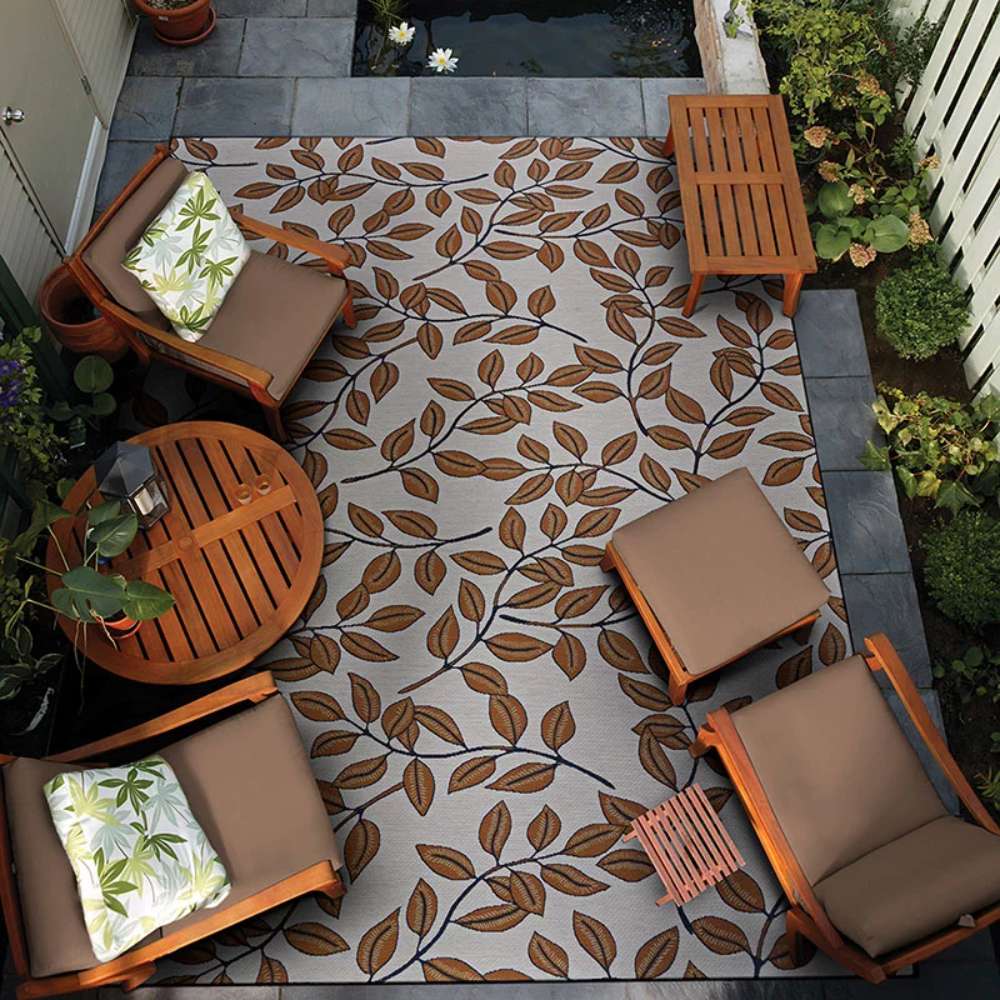 A cozy patio setup with chairs and a table sits atop Couristan Dolce Indoor/Outdoor Rug - Summer Ivy/Ivory-Terra-Cotta