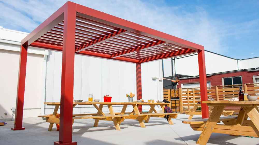 A cozy seating nook with two chairs sits peacefully under a white Structureworks Element Trex Pergola on a standalone raised deck in a grassy yard