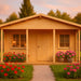 A cozy wooden cabin surrounded by colorful flowers at sunset is the GardenHouse24 USA Vienna 70 Garden Room, perfect for a tranquil backyard retreat