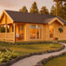 A cozy wooden cabin with a front porch and large glass doors sits in a landscaped garden, showcasing the GardenHouse24 USA Garda 90 Garden Room