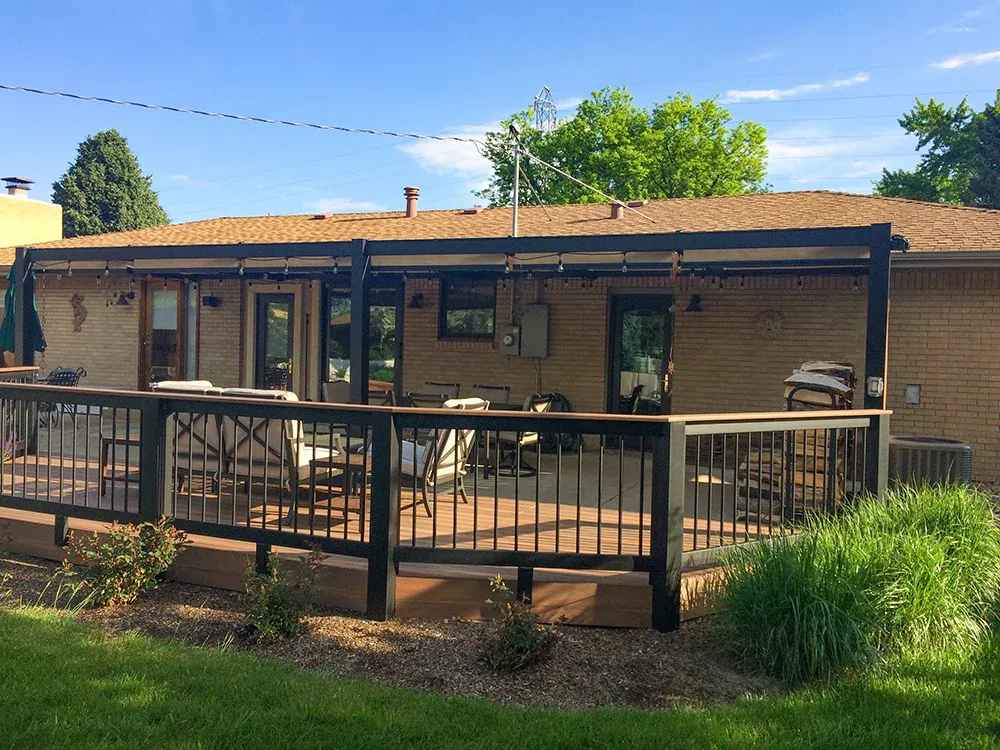 A dark-framed Structureworks Outlook Aluminum Patio Cover & Pergola extends over a wooden deck with a black railing