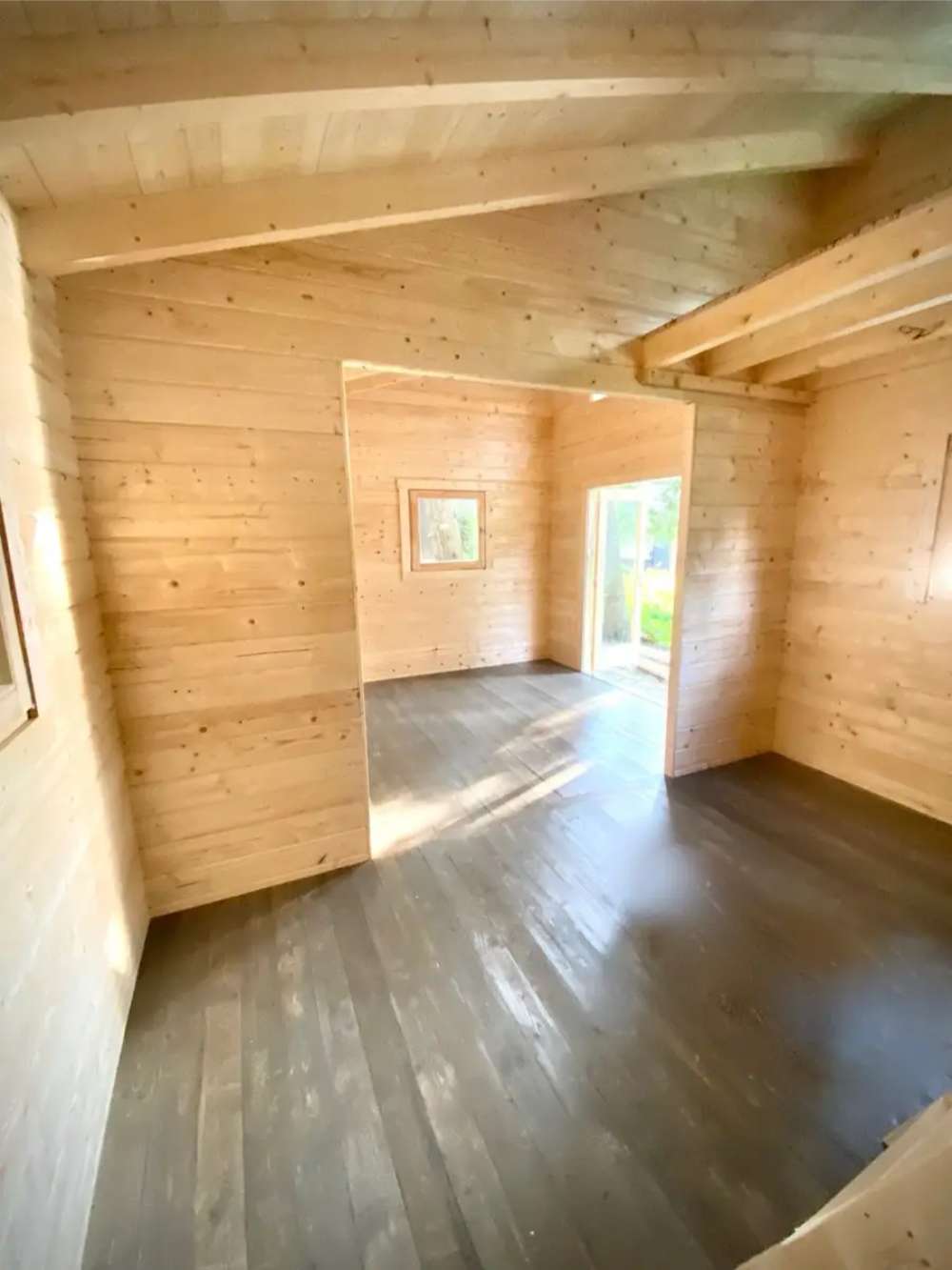 A different angle of the unfinished Sawmill Structures The Versa 240 70MM Garden Room shows two connected open spaces with natural wood walls and floors