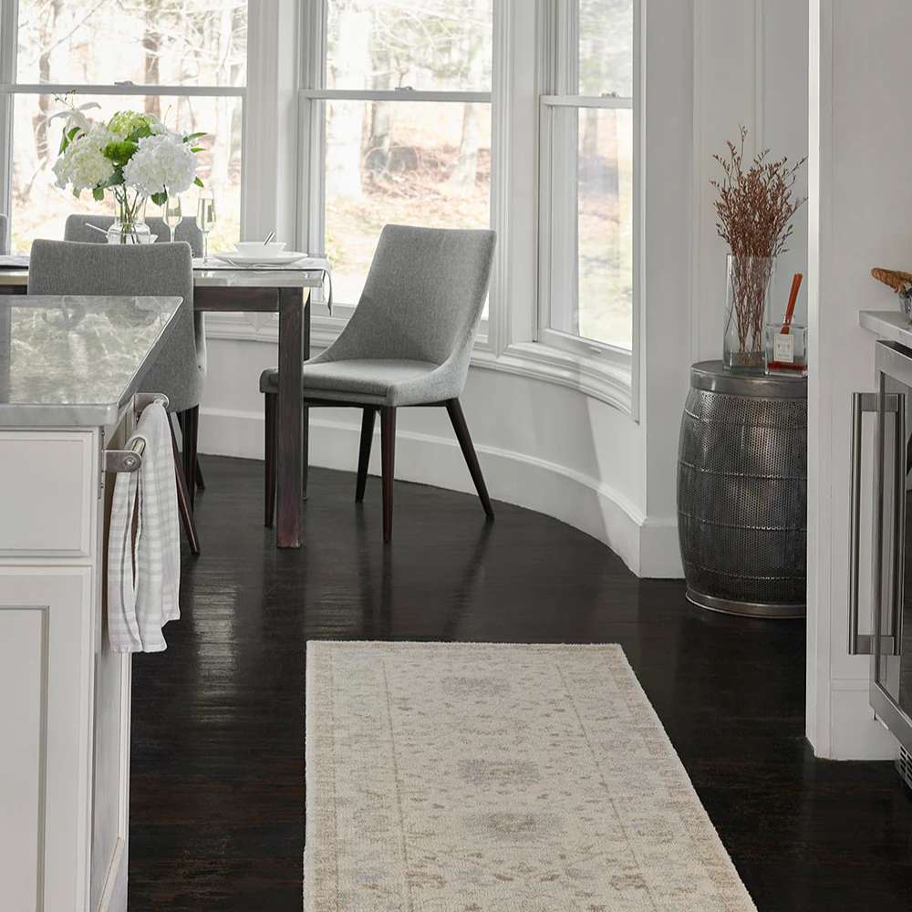 A dining area with sleek gray chairs is grounded by Momeni Anatolia Indoor Rug - ANA-5 Beige