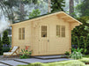 A full exterior view of the Sawmill Structures Harvest Grand Bungalow 107 Garden Room surrounded by greenery and featuring a small porch and lounge chair