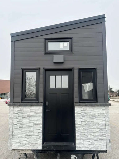 A head-on view of the Sawmill Structures Wanderlove Tiny Home highlights its symmetrical design with a central black door and matching side windows