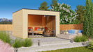 A landscaped backyard scene features the GardenHouse24 USA Q Bic ALU 44A Garden Room furnished with cozy seating and surrounded by greenery and a mountain backdrop