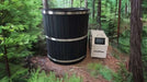 A large, black circular cold plunge tub with metal bands stands in a forest beside a white cooling unit labeled “ChillFlex,” part of Sawmill Structures Chiller Plunge setup