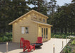 A light wood cabin with a sloped roof, glass double doors, and red chairs on a deck is the Sawmill Structures The Versa 160 Atrium 70MM Garden Room nestled in a forest