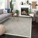 A living room with a sofa, chair, and plants displays Couristan Liguria Indoor/Outdoor Rug - Noli/Dove Grey as the centerpiece on a dark wood floor