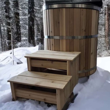 A natural wood version of Sawmill Structures Chiller Plunge is shown outdoors in the snow with matching wooden steps leading up to it