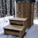 A natural wood version of Sawmill Structures Chiller Plunge is shown outdoors in the snow with matching wooden steps leading up to it