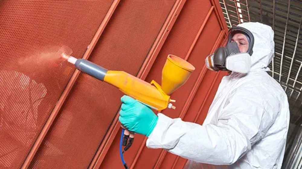 A person in protective gear is powder coating a metal panel, showing the durable finish applied to the Structureworks Breeze Aluminum Pergola frames