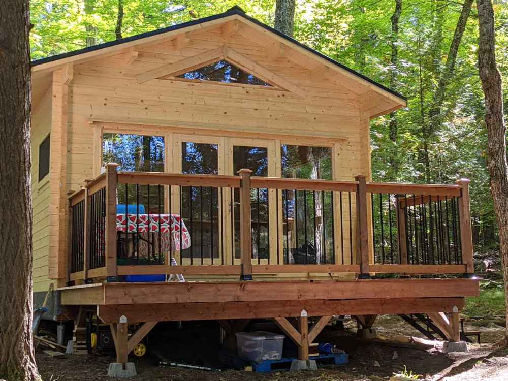 A raised deck with black railing leads to the glass double doors of the Sawmill Structures Edwin Lake House 70MM Garden Room