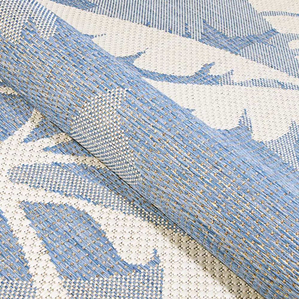 A rolled section of Couristan Monaco Indoor/Outdoor Rug - Coastal Flora/Ivory-Sapphire reveals its flexible, durable weave and rich texture