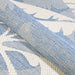 A rolled section of Couristan Monaco Indoor/Outdoor Rug - Coastal Flora/Ivory-Sapphire reveals its flexible, durable weave and rich texture