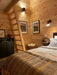 A rustic bedroom with a wooden ladder leading to a loft and warm-toned blankets showcases the inviting interior of the Sawmill Structures The Jumbo Grand Loft 130 SD Garden Room