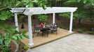 A secluded forest patio features a black dining table and chairs shaded by a white Structureworks Trex Pergola