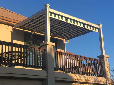 A second-story balcony is shaded by a striped retractable awning within a sleek, white-framed Structureworks Craftsman Aluminum Patio Cover & Pergola