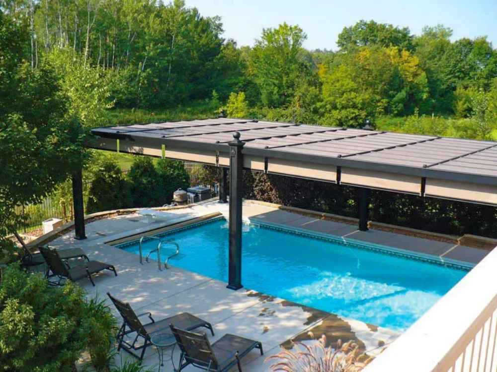 A sleek, modern poolside area with loungers shaded by a long, dark-colored Structureworks Windsor Aluminum Patio Cover