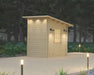 A small wooden Sawmill Structures Loo Loo House Garden Room glows with soft exterior lights at dusk