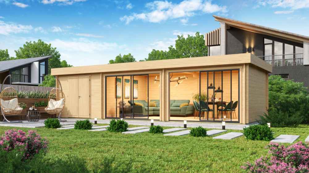 A stylish GardenHouse24 USA ALU Concept 70L Garden Room sits in a landscaped yard, with floor-to-ceiling windows revealing a cozy interior with green sofas and a dining set