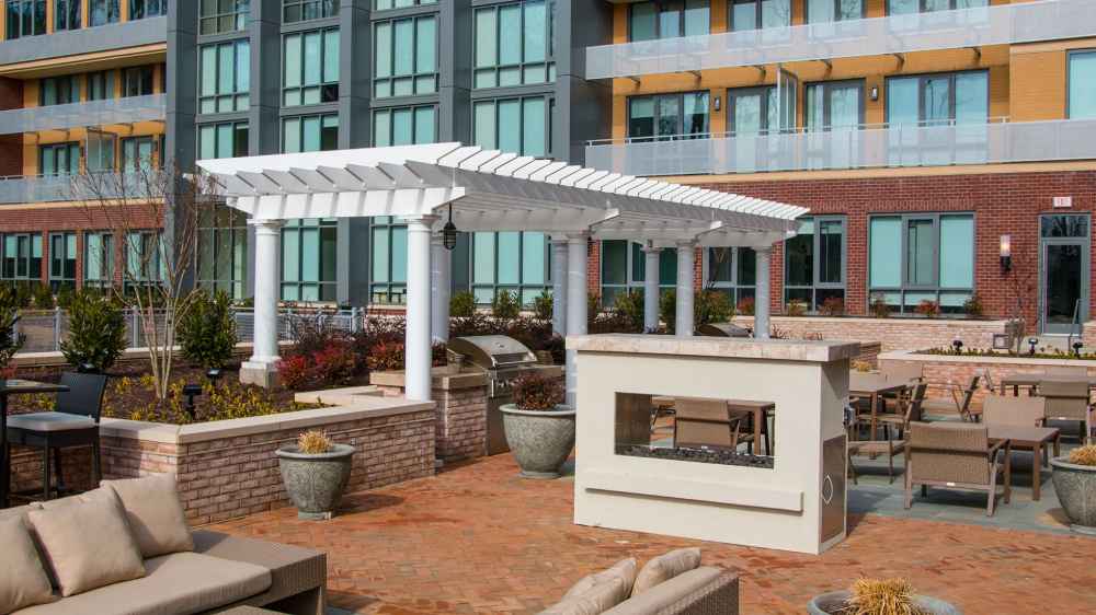 A stylish apartment courtyard includes a white Structureworks Trex Pergola beside a fire feature and lounge seating