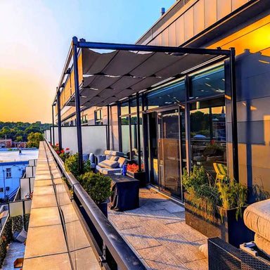 A sunset view enhances a rooftop deck with a contemporary Structureworks Silhouette Aluminum Patio Cover & Pergola over lounge furniture and potted plants