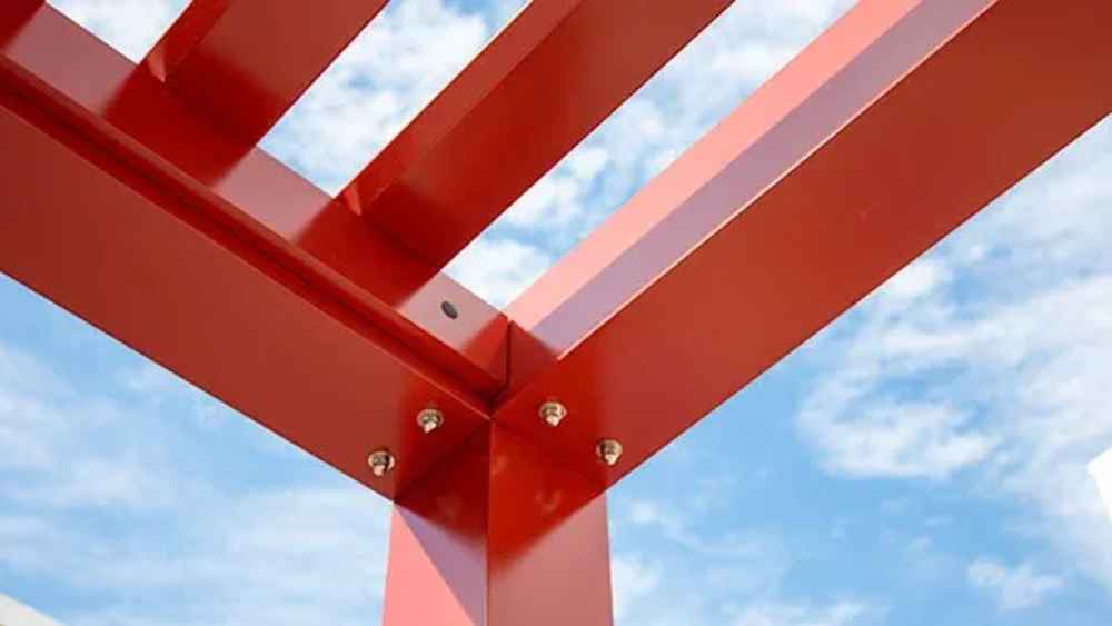 A top-down view shows a bold red Structureworks Element Trex Pergola casting striped shadows over picnic tables on a concrete patio