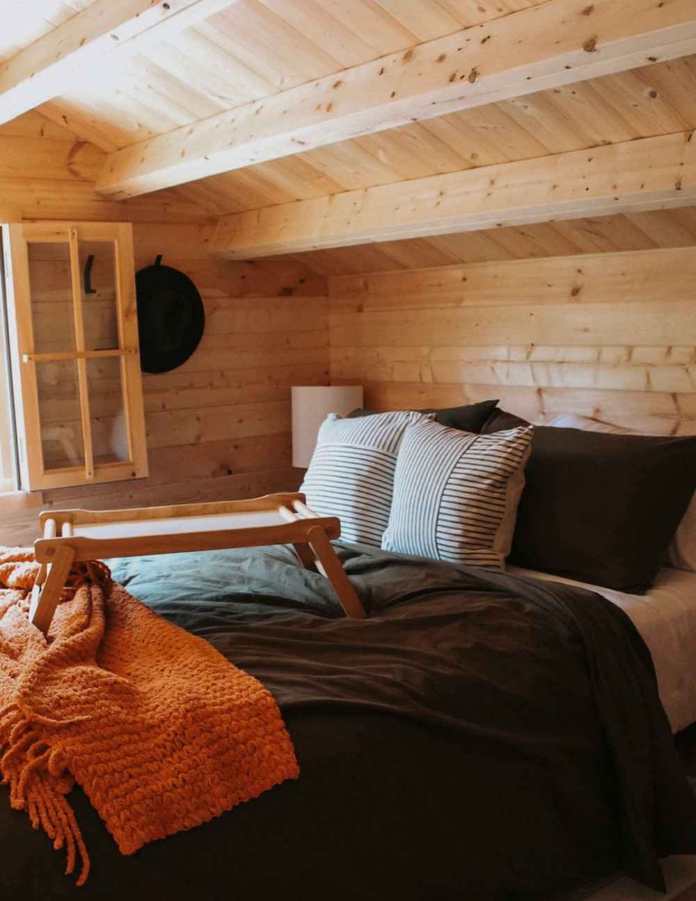 A warm, intimate bedroom with a sloped ceiling, striped pillows, and an orange blanket illustrates the upper-level sleeping nook in the Sawmill Structures BlueWater Loft 160 38mm Garden Room