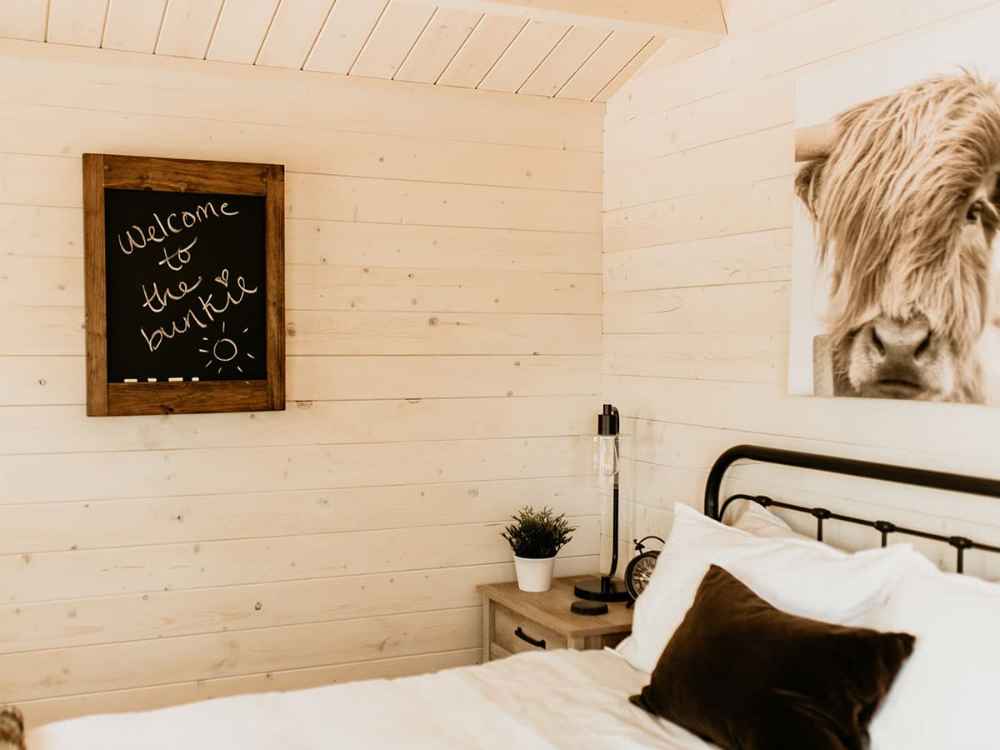 A welcoming sign on a chalkboard and rustic decor above a bed in the Sawmill Structures Harvest Grand Bungalow 107 Garden Room