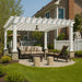 A white Structureworks Williamsburg Fiberglass Pergola provides shade over a cozy outdoor lounge area with couches and a lamp hanging from the center