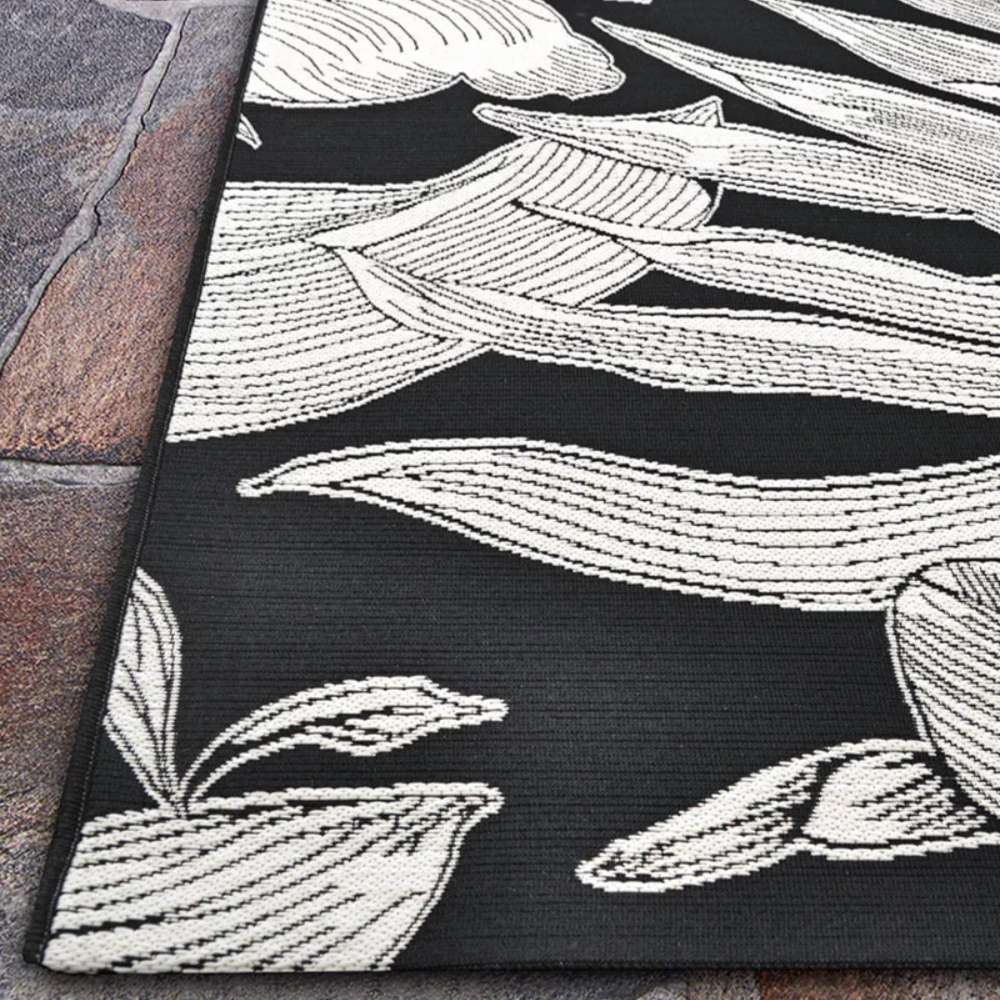 A wide corner shot of Couristan Dolce Indoor/Outdoor Rug - Flora/Nero displays its clean edges and prominent white flowers spreading across the black base