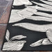 A wide corner shot of Couristan Dolce Indoor/Outdoor Rug - Flora/Nero displays its clean edges and prominent white flowers spreading across the black base