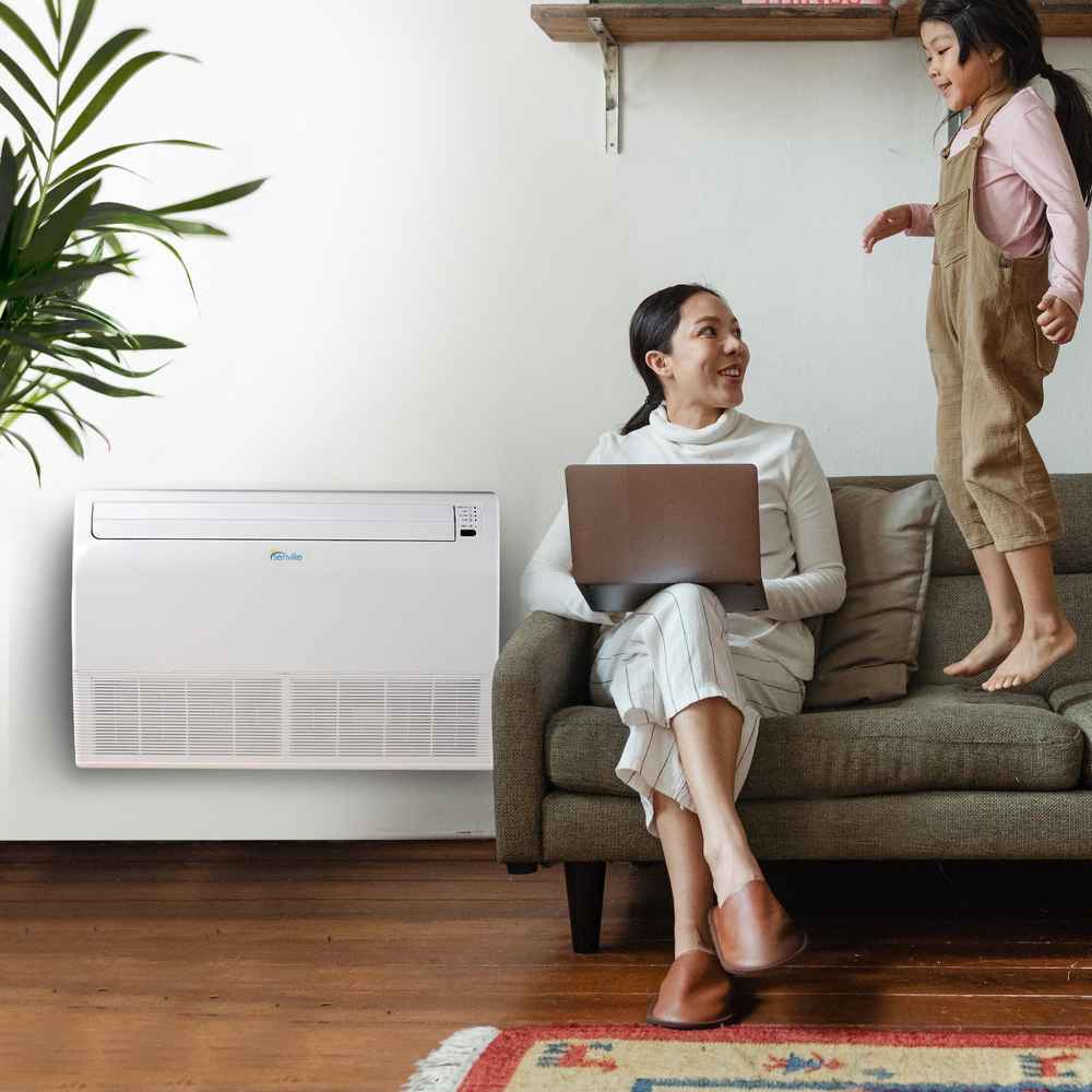 A woman with a laptop and a child in a living room with the Senville 18000 BTU Floor Mounted Mini Split Air Conditioner - Heat Pump - SENA18HFIF installed on the wall