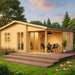 A wooden GardenHouse24 USA Skanderborg 90 Garden Room with a shaded patio and outdoor dining set is shown surrounded by lush greenery