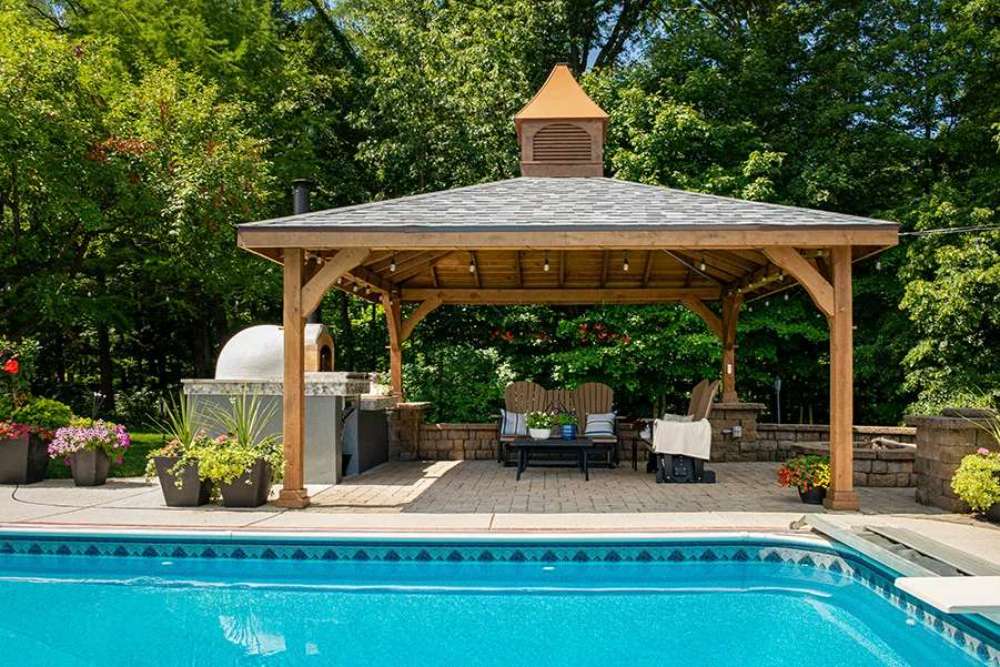 A beautiful outdoor setting featuring the Brookside Timber Frame Forest Melody Pavilion by a poolside