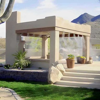 A beige outdoor gazebo surrounded by plants uses the Aeromist Pinnacle 1000 PSI Misting System to release a fine mist from the roof edges